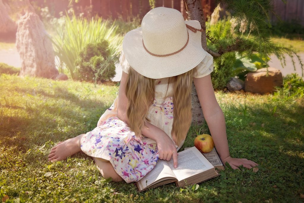 Image d'une enfant en train de lire un livre dans le jardin avec son chapeau.
